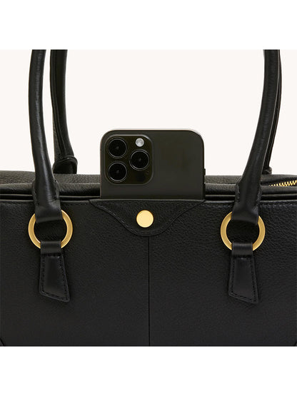 A black smartphone is partially inserted into an exterior pocket of the Hammitt Los Angeles Meredith Small in Black/Brushed Gold handbag.