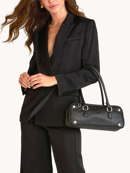A person in a black suit carries the Hammitt Los Angeles Meredith Small in Black/Brushed Gold handbag over their arm.