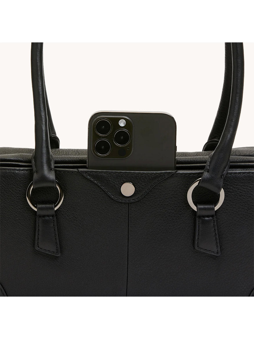 A black smartphone peeks from the exterior pocket of the Hammitt Los Angeles Meredith Small in Black/Gunmetal, a pebble leather doctor-style bowling bag with two handles.