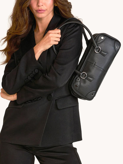 A woman in a black suit holds the Hammitt Los Angeles Meredith Small in Black/Gunmetal, a crossbody-ready pebble leather handbag, over her shoulder against a plain background.
