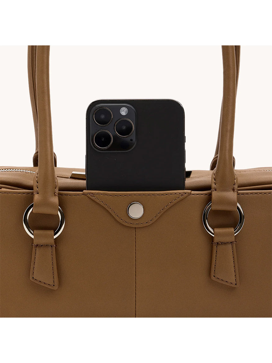 A black smartphone is partially visible in the exterior pocket of the Hammitt Los Angeles Meredith Small in Dune/Silver, a brown leather bag with two handles and silver rings.
