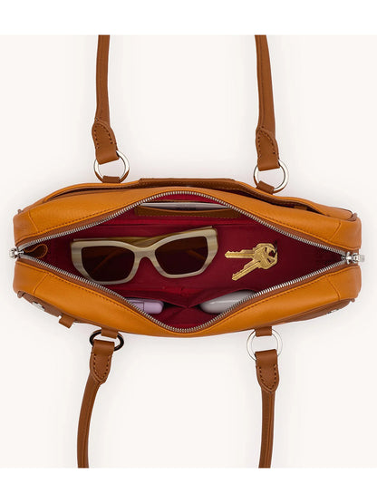 The Hammitt Los Angeles Meredith Small in Tailored Tangerine/Silver is unzipped and viewed from above, revealing a pair of sunglasses, a set of keys, and a small cylindrical item inside its red interior.