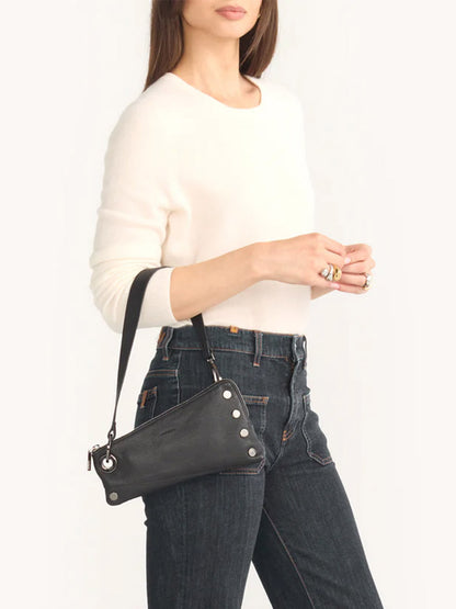 A person wearing a white sweater and dark jeans is elegantly holding a Hammitt Los Angeles Nash Pochette in Black/Gunmetal, adorned with silver buttons.