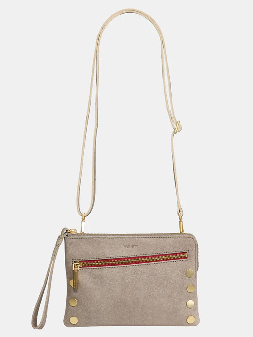 The Hammitt Los Angeles Nash Small Clutch in Pewter is a stylish crossbody bag with a thin adjustable and convertible strap. It features a front zippered pocket accented with red detailing and gold-tone metal studs at the bottom corners.