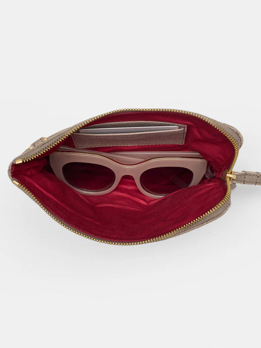 Open the Hammitt Los Angeles Nash Small Clutch in Pewter to reveal a zippered pouch lined with red fabric, showcasing a pair of sunglasses and a small wallet inside, and featuring a convertible strap for versatile carrying options.