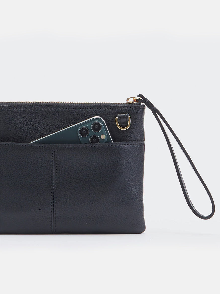 The Hammitt Los Angeles Nash Small Clutch in Black with Brushed Gold and Red Zip is a leather wristlet pouch featuring a zippered top and a small external pocket that holds a green smartphone. It also comes with a removable crossbody strap for added convenience.