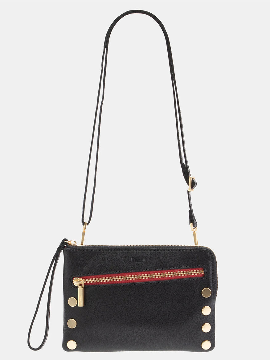 A Hammitt Los Angeles Nash Small Clutch in black leather with brushed gold button accents, a front zip pocket featuring red trim, a gold zipper, and an adjustable convertible strap.