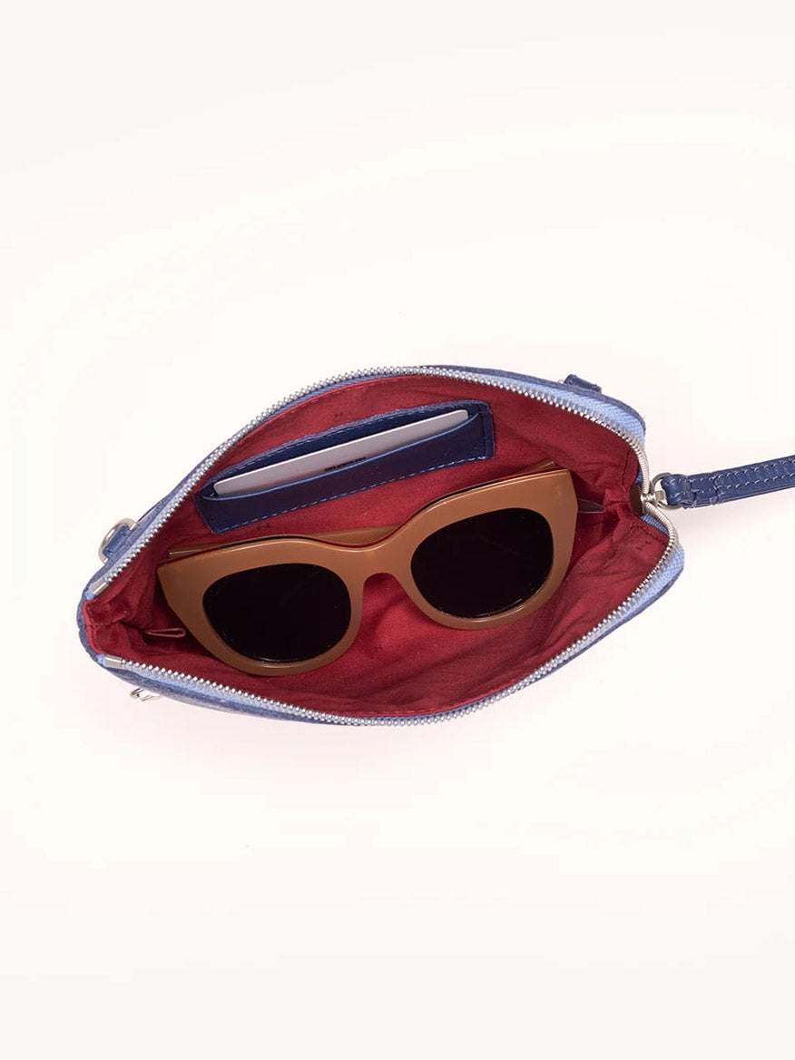 Open the Hammitt Los Angeles Nash Small Clutch in Jazz Blues, featuring a red interior. It contains a pair of brown sunglasses and a blue cardholder, all crafted from pebbled leather.