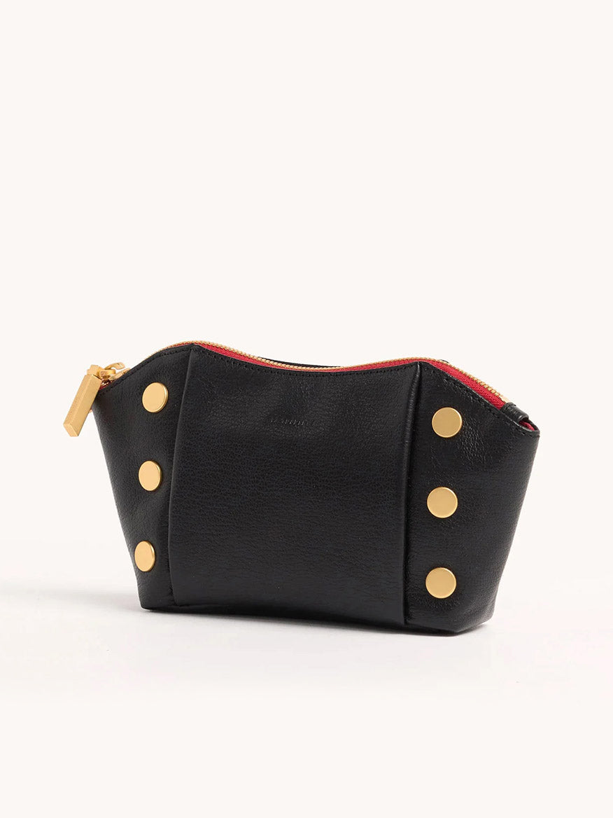 The Hammitt Los Angeles Paul Pocket in Black Press/Brushed Gold is a mini evening clutch in Italian calf leather, featuring gold-tone button accents, a red zipper, and a gold zipper pull against a sleek black background.