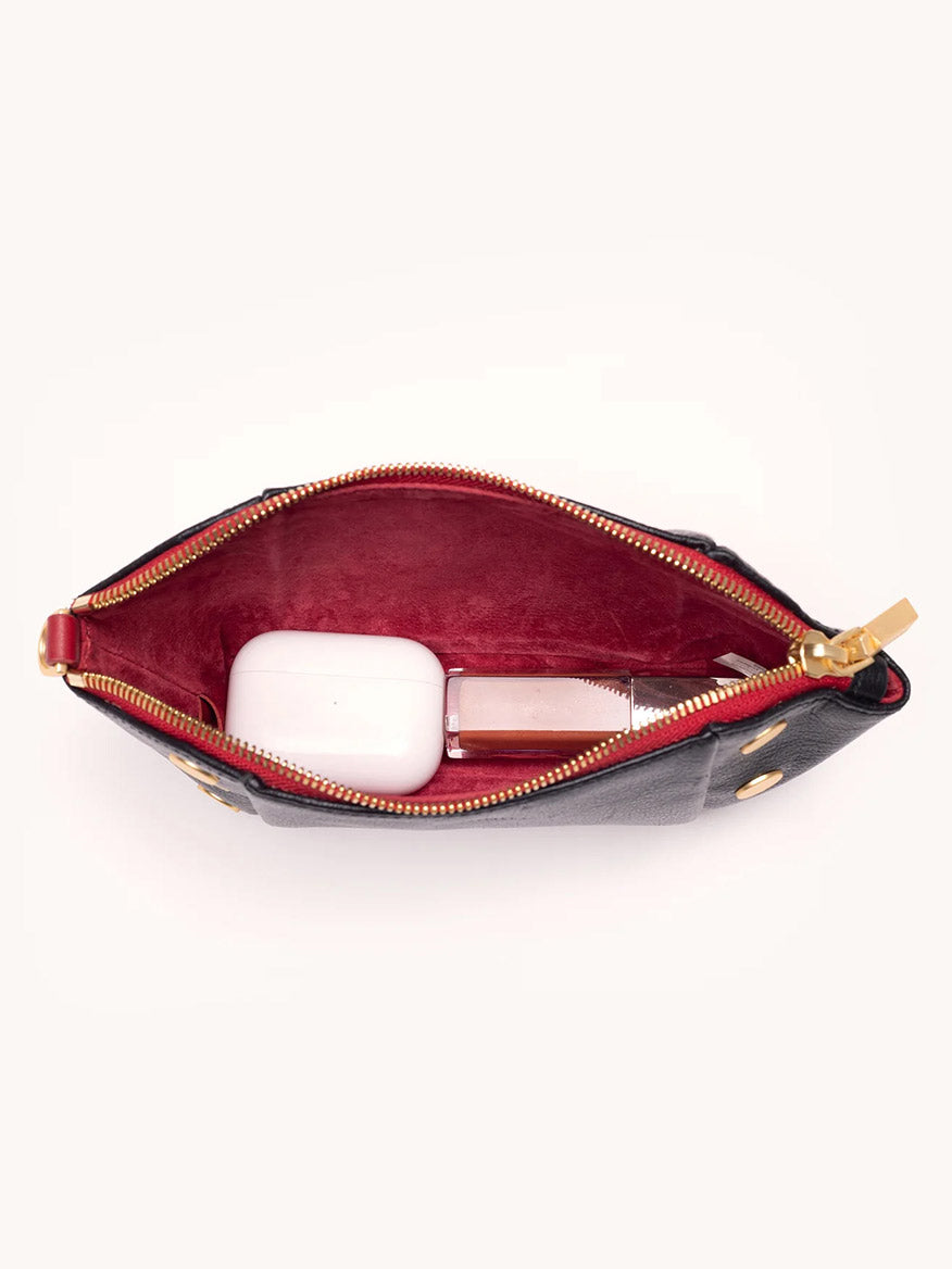 The Hammitt Los Angeles Paul Pocket in Black Press/Brushed Gold features Italian calf leather with a red interior—unzipped to reveal a white case and rectangular bottle, making it the perfect mini evening clutch for your essentials.