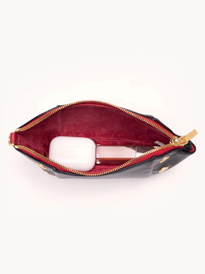 The Hammitt Los Angeles Paul Pocket in Black Press/Brushed Gold features Italian calf leather with a red interior—unzipped to reveal a white case and rectangular bottle, making it the perfect mini evening clutch for your essentials.