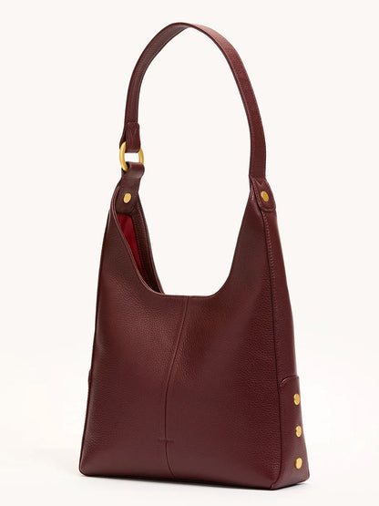 The Hammitt Los Angeles Tim Med Hobo in Cherrywood Pebble/Brushed Gold is a structured, rectangular oxblood red leather shoulder bag with a wide strap and gold hardware, displayed against a plain background.