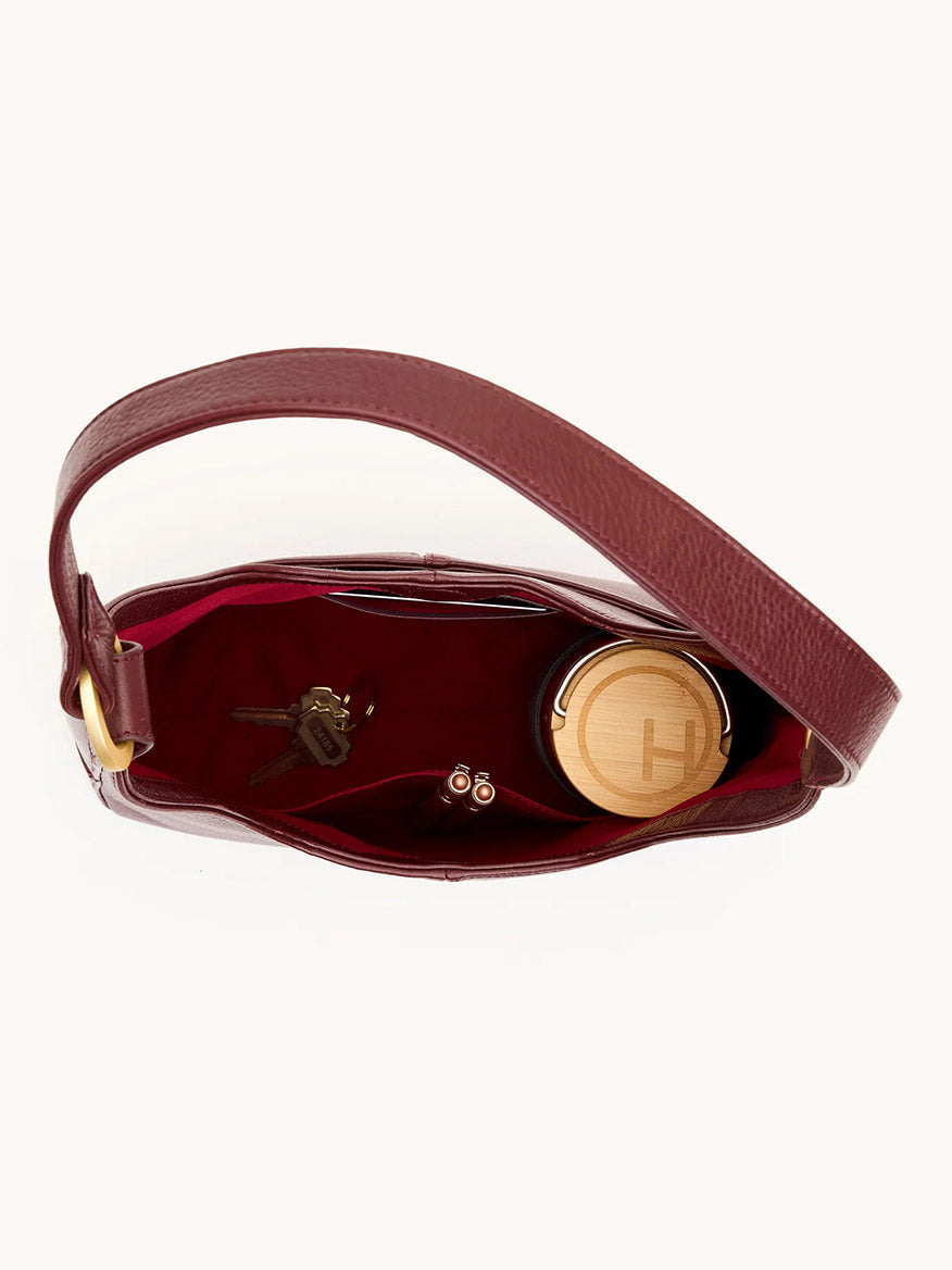 Top view of an open Hammitt Los Angeles Tim Med Hobo in Cherrywood Pebble/Brushed Gold containing keys, a cylindrical container with a wooden lid, and two lipsticks inside.