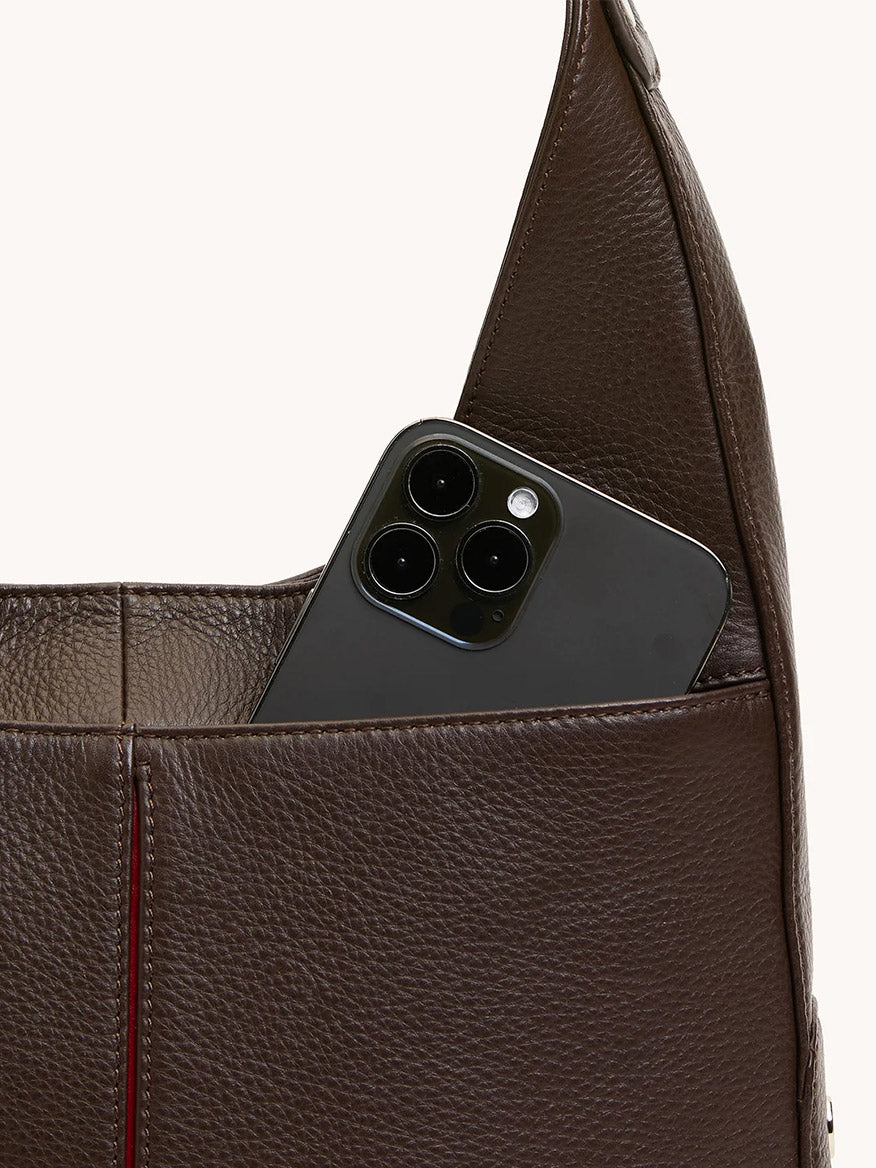 A dark smartphone peeks out of the front pocket of the Hammitt Los Angeles Tim Med Hobo in Espresso Pebble/Silver, crafted from textured dark espresso brown leather.