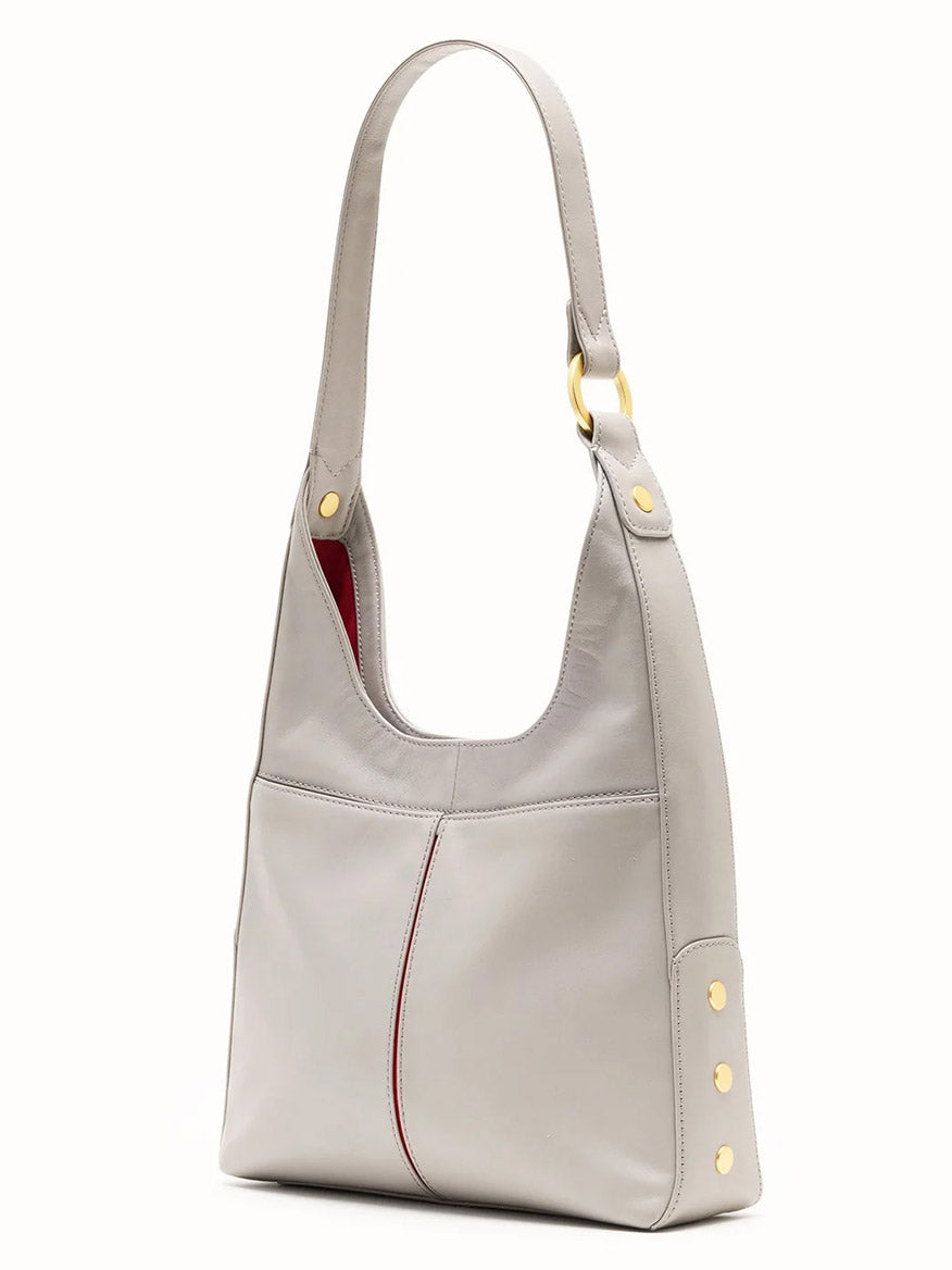 The Hammitt Los Angeles Tim Med Hobo in Stormy/Brushed Gold features a light gray finish, gold-tone hardware, red interior accents, and a wide strap, displayed upright against a plain background.