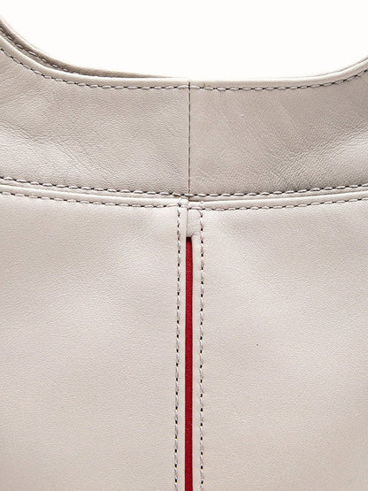 Close-up view of the Hammitt Los Angeles Tim Med Hobo in Stormy/Brushed Gold, showcasing its light gray pebble leather surface with visible stitching and a vertical seam accented by a thin red stripe.