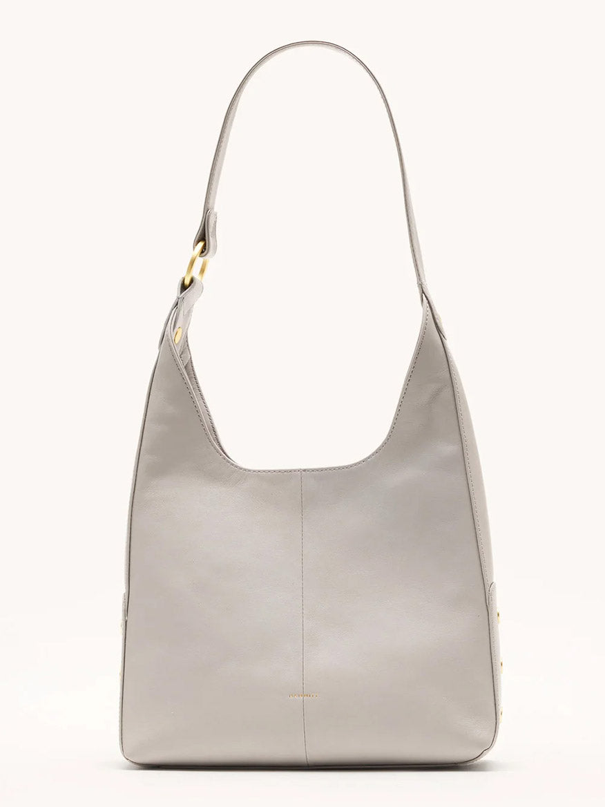 The Hammitt Los Angeles Tim Med Hobo in Stormy/Brushed Gold is a minimalist, light gray pebble leather bag with a wide strap and gold-tone hardware, displayed upright against a plain background.