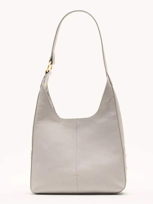 The Hammitt Los Angeles Tim Med Hobo in Stormy/Brushed Gold is a minimalist, light gray pebble leather bag with a wide strap and gold-tone hardware, displayed upright against a plain background.