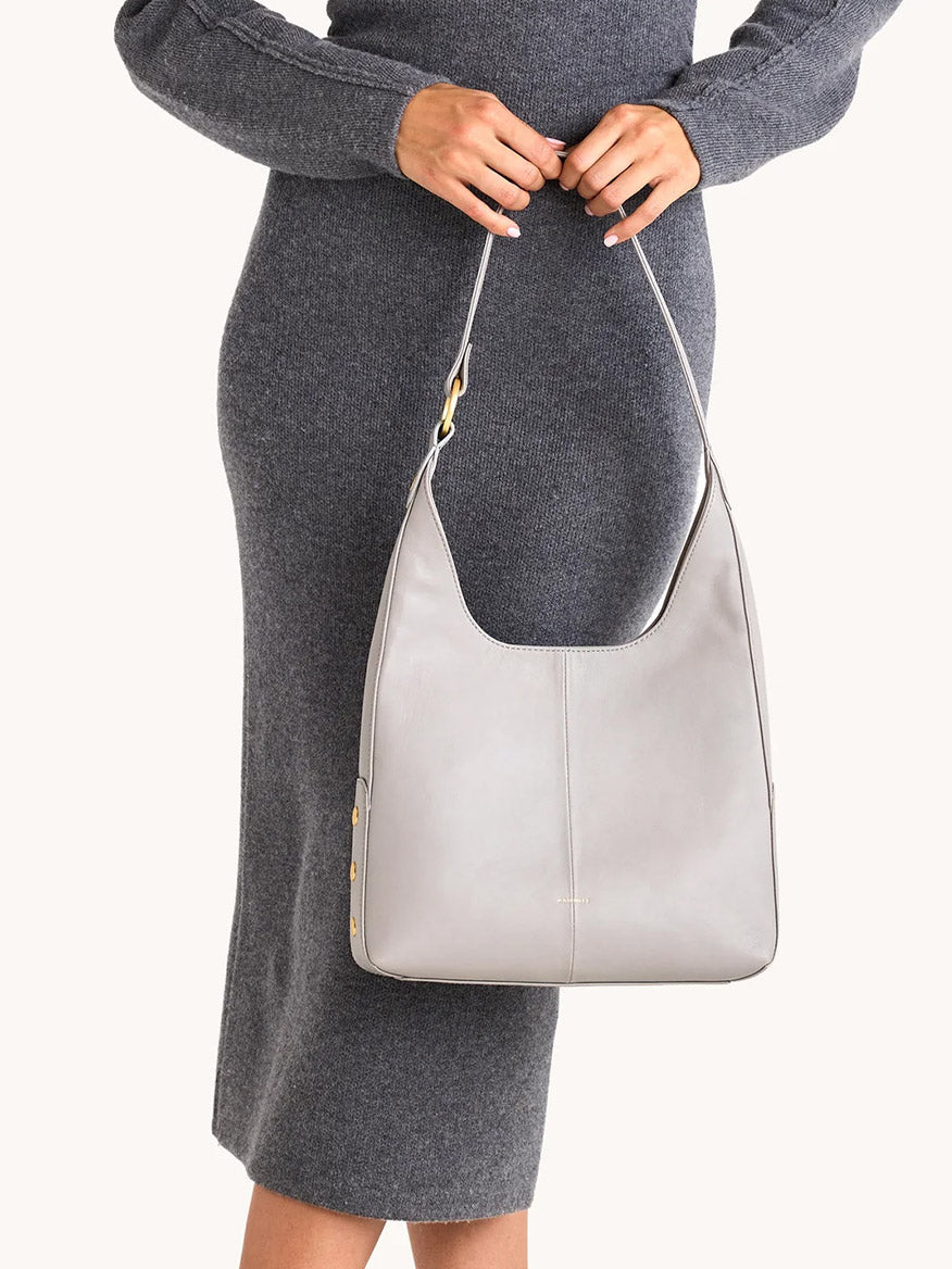 A person in a gray knit dress holds the Hammitt Los Angeles Tim Med Hobo in Stormy with brushed gold accents.