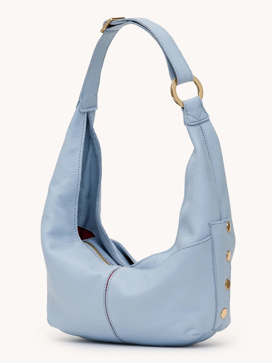 The Hammitt Los Angeles Tom Zip Medium in Hazy Blue/Gold is a compact hobo bag with pebbled leather, gold hardware, side button details, and an adjustable shoulder strap, shown against a plain background.