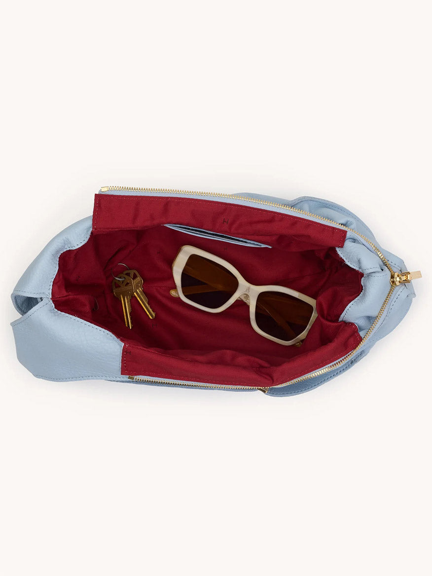 The Hammitt Los Angeles Tom Zip Medium in Hazy Blue/Gold is a compact pebbled leather hobo bag with a red interior, adjustable shoulder strap, and holds sunglasses and keys for daily convenience.