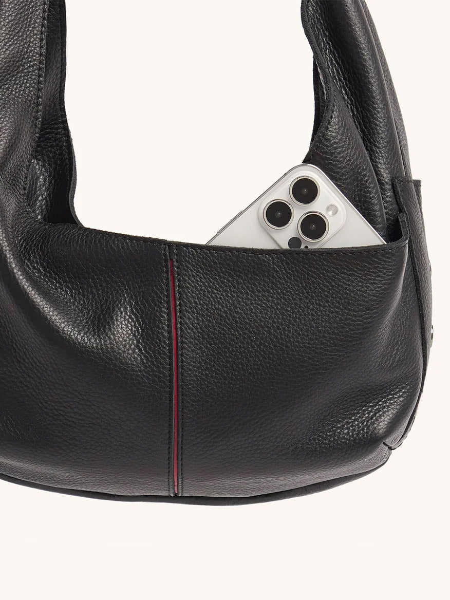 A white smartphone with three cameras peeks out from the outer pocket of the Hammitt Los Angeles Tom Zip Medium in Black/Gunmetal, a black pebbled leather hobo bag with an adjustable shoulder strap.
