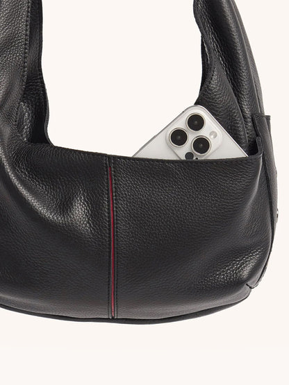 A white smartphone with three cameras peeks out from the outer pocket of the Hammitt Los Angeles Tom Zip Medium in Black/Gunmetal, a black pebbled leather hobo bag with an adjustable shoulder strap.