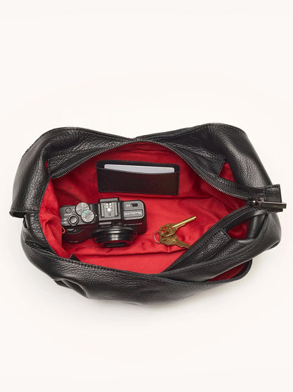The Hammitt Los Angeles Tom Zip Medium in Black/Gunmetal is a black pebbled leather hobo bag with a red interior, adjustable shoulder strap, and enough space to hold a camera, wallet, and key.