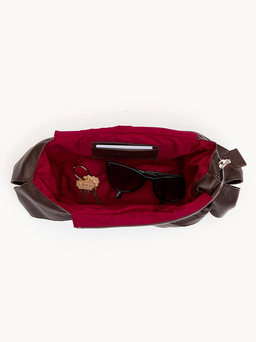 The Hammitt Los Angeles Tom Zip Medium in Espresso Pebble/Silver holds black sunglasses, a set of keys with a leather keychain, and a slim smartphone, all against its striking red interior.