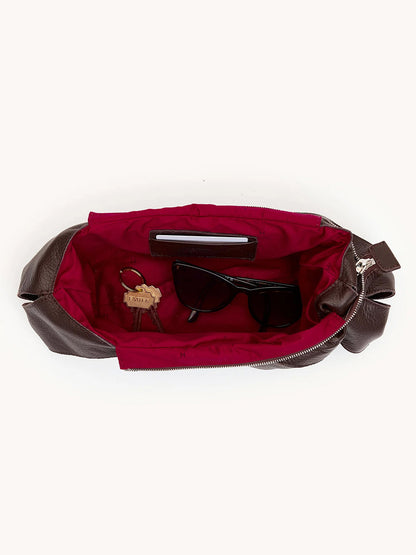 The Hammitt Los Angeles Tom Zip Medium in Espresso Pebble/Silver holds black sunglasses, a set of keys with a leather keychain, and a slim smartphone, all against its striking red interior.