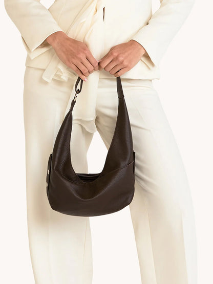 A person in an off-white suit holds the Hammitt Los Angeles Tom Zip Medium in Espresso Pebble/Silver by its strap in front of their body.
