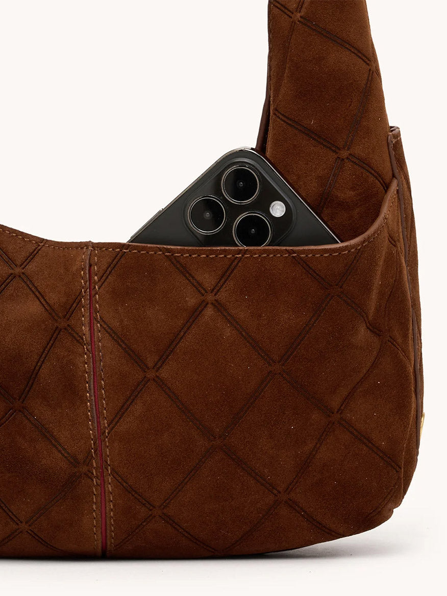 A black smartphone peeks from the outer pocket of the Hammitt Los Angeles Tom Zip Medium in Chocolate Diamond Suede/Antique Gold, featuring a soft quilted finish and an adjustable shoulder strap.