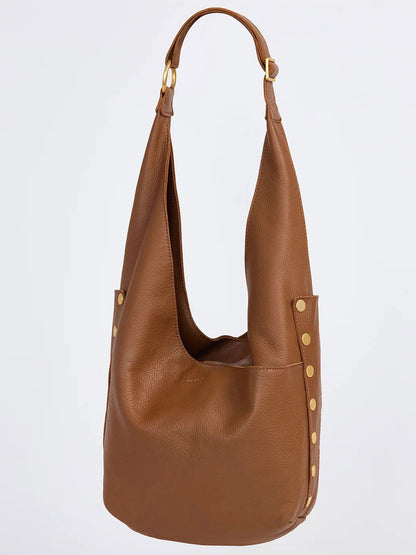 The Hammitt Los Angeles Tom Zip in Mahogany Pebble is a brown pebbled leather hobo bag featuring a slouchy design, gold rivet accents on the sides, and a single adjustable strap.