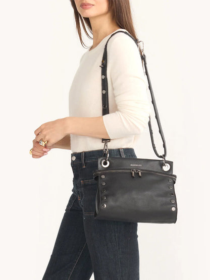 A person in a white sweater and jeans carries the Hammitt Los Angeles Tony Signature Medium Crossbody in Black & Gunmetal, elegantly draped over their shoulder.