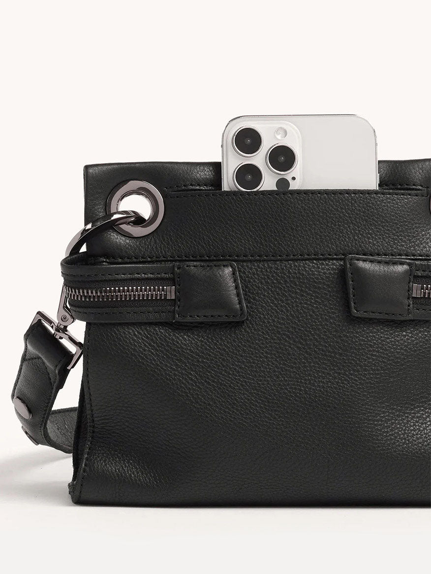 The Hammitt Los Angeles Tony Signature Small Crossbody in Black showcases pebbled leather and metal ring details, featuring an adjustable strap. A smartphone with a triple-lens camera is visible from the top.