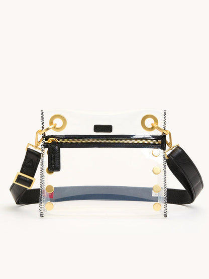 The Hammitt Los Angeles Tony Small Crossbody Bag in Clear Black/Brushed Gold features stadium-approved acrylic, TPU and leather trim, gold hardware, a front zipper pocket, and an adjustable strap, shown against a plain background.
