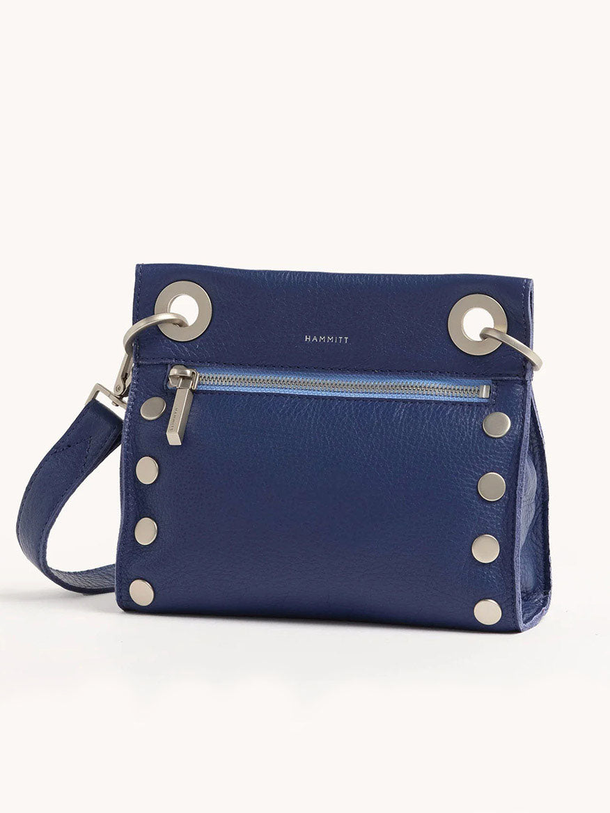 The Hammitt Los Angeles Tony Small Crossbody Bag in Jazz Blues is a chic blue pebbled leather handbag featuring silver grommets and studs, a front zipper pocket, and an adjustable shoulder strap for versatile crossbody wear.