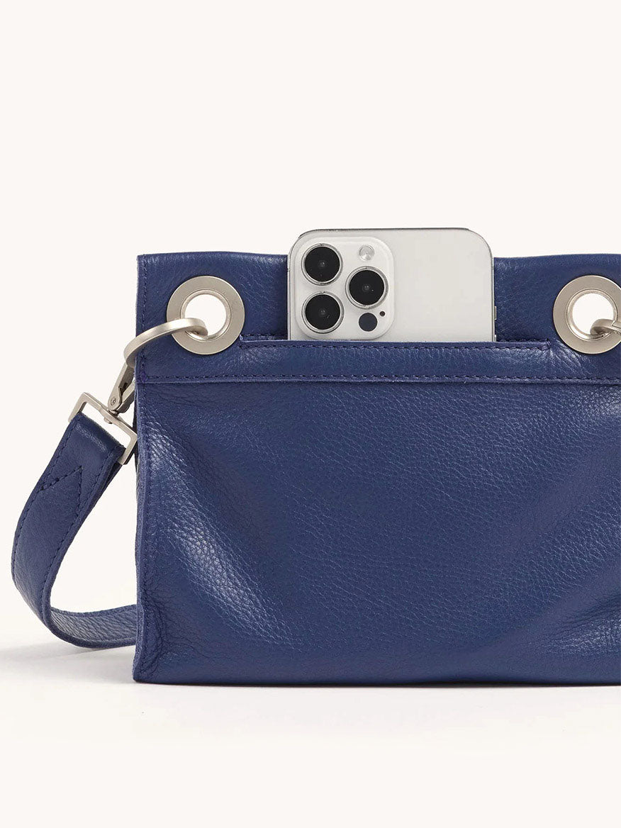 A smartphone peeks from the Hammitt Los Angeles Tony Small Crossbody Bag in Jazz Blues, featuring metal eyelets and an adjustable strap.