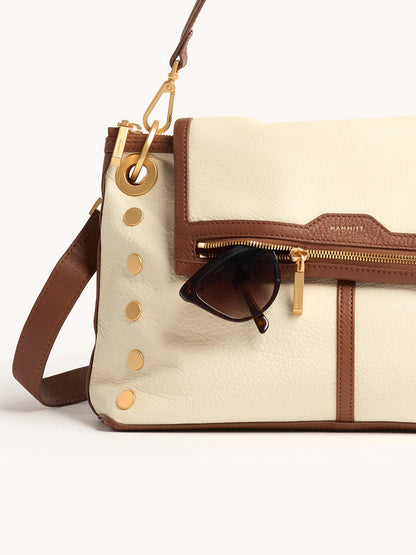 The Hammitt Los Angeles VIP Grand in Courtyard Cream is a cream and brown leather crossbody with gold hardware, inspired by signature styles, featuring a pair of sunglasses hooked onto its front pocket.