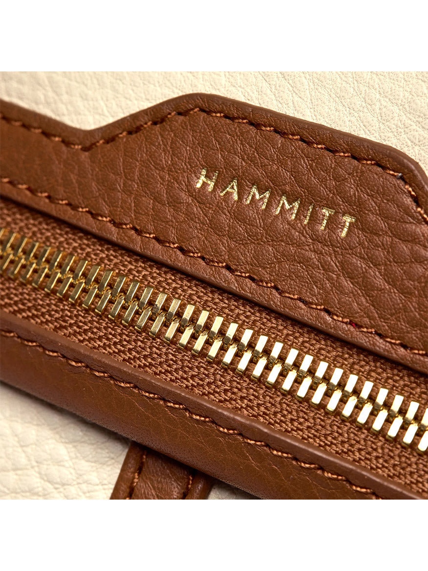 Close-up of a brown leather zipper with gold teeth on the Hammitt Los Angeles VIP Grand in Courtyard Cream, featuring "HAMMITT" embossed in gold above the zipper—an iconic Hammitt detail.