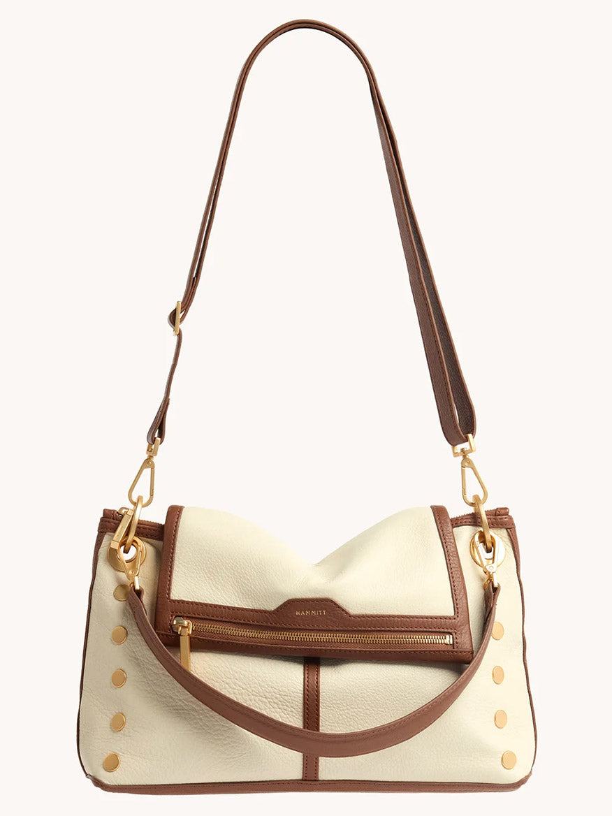 The Hammitt Los Angeles VIP Grand in Courtyard Cream is a cream and brown leather crossbody bag with gold hardware, front zip pocket, decorative gold studs, adjustable strap, and signature VIP Grande-inspired style.