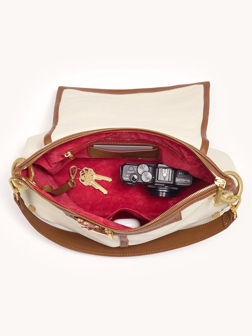 The Hammitt Los Angeles VIP Grand in Courtyard Cream crossbody, shown unzipped with a camera, keys, and wallet inside, highlights its cream and brown exterior plus signature red lining—classic Hammitt style.
