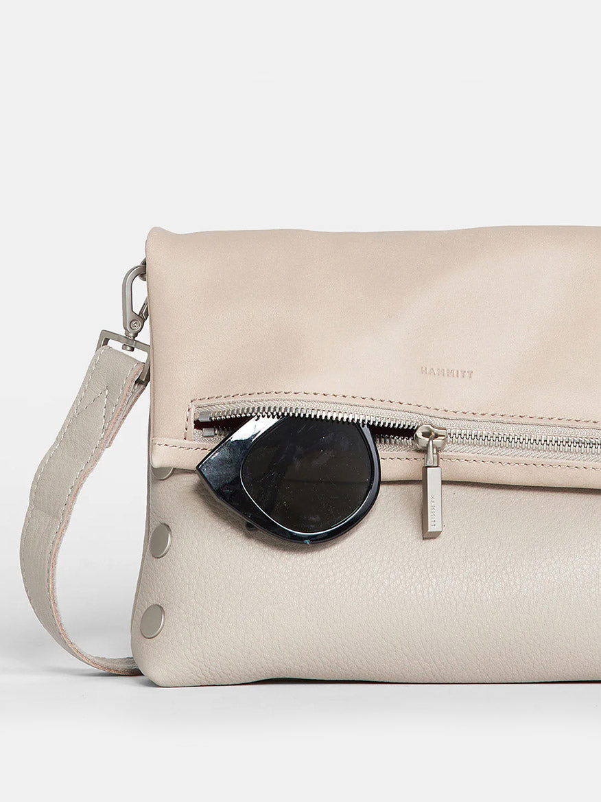 Paved Grey pebbled leather clutch with a diagonal zipper and sunglasses tucked under the strap on a plain background.