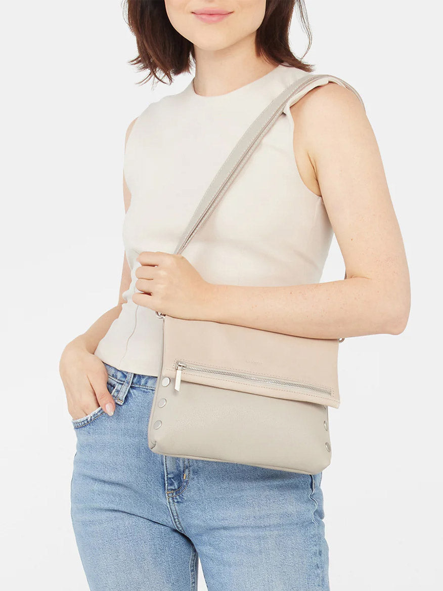 A woman in a sleeveless top and jeans wearing a Hammitt Los Angeles VIP Medium Clutch in Paved Grey.