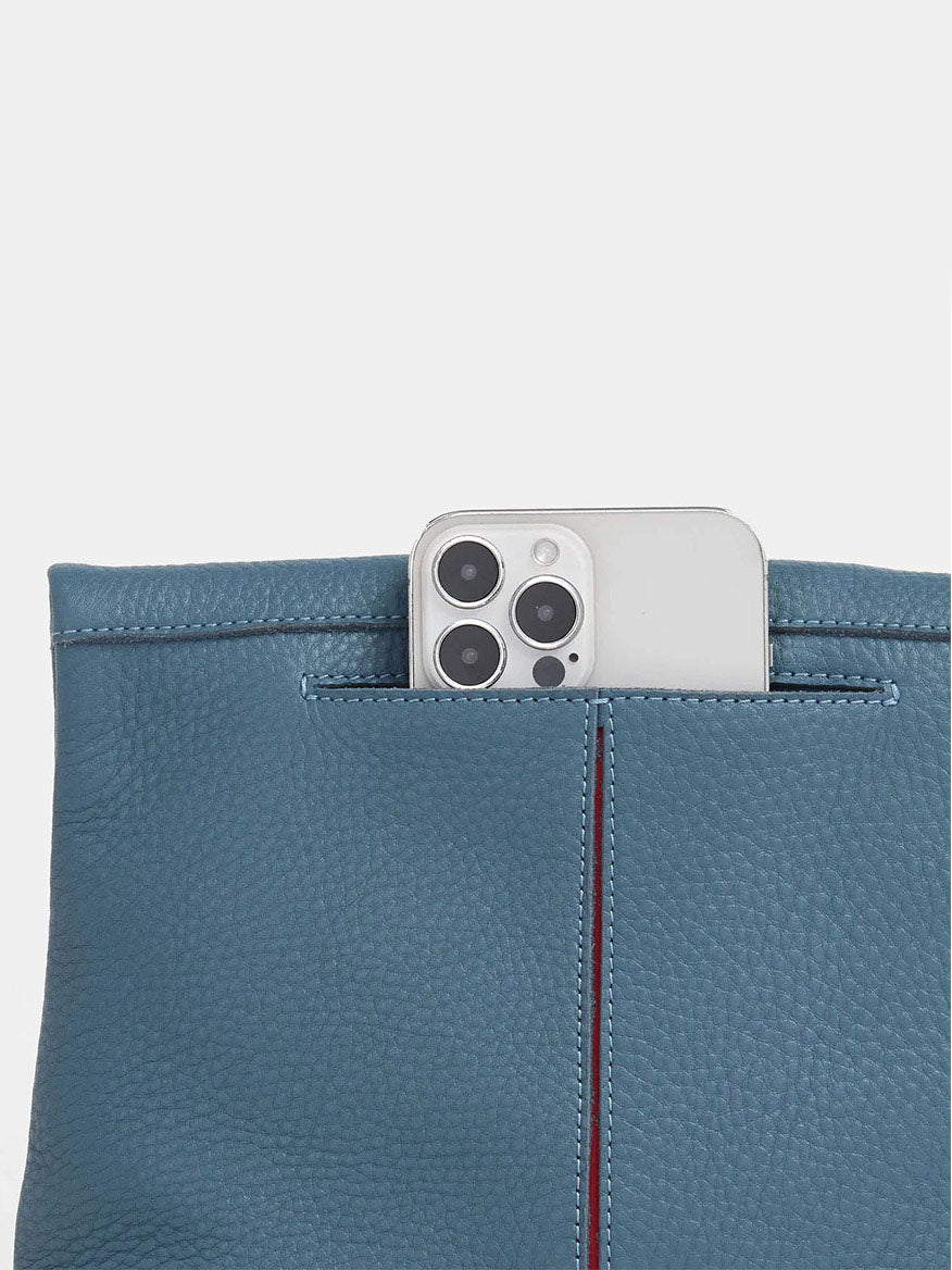 A smartphone with a triple-lens camera is partly tucked into the Hammitt Los Angeles VIP Medium Clutch in Curated Blue leather.