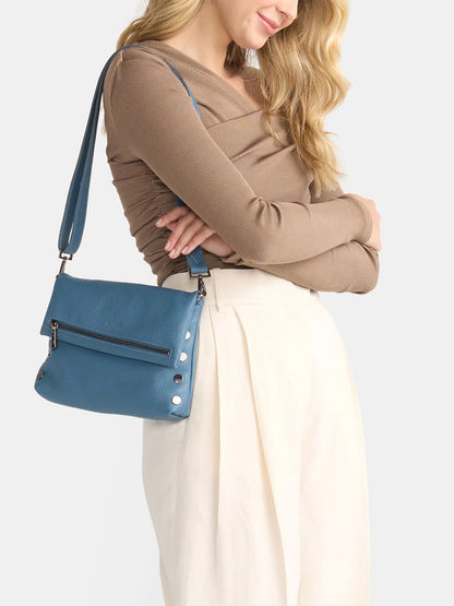 Someone wearing a light brown top and white pants is carrying a Hammitt Los Angeles VIP Medium Clutch in Curated Blue with silver accents and a removable crossbody strap.