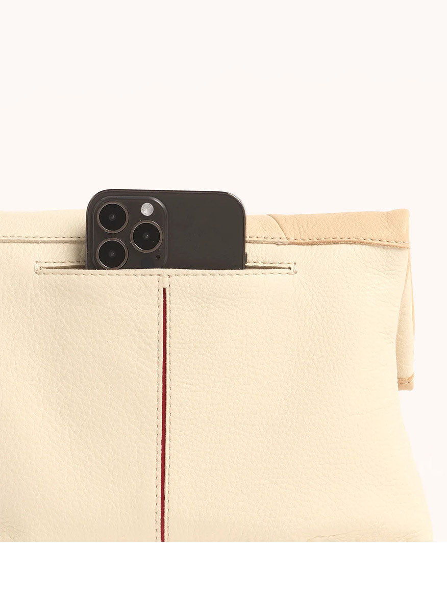 A smartphone partially inserted into a pocket of a light beige leather bag, reminiscent of the serene hues of Hammitt Los Angeles VIP Medium Clutch in Coastal Cream.