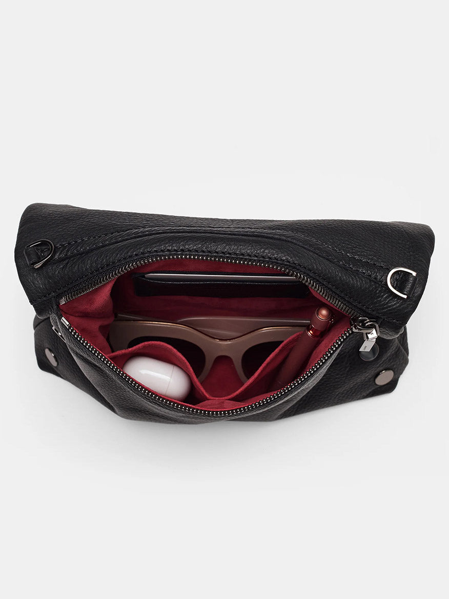 Reveal the versatility of the Hammitt Los Angeles VIP Medium Clutch in Black. This open black pebbled leather bag comes with a red interior and an adjustable crossbody strap. Inside, you'll find it spacious enough to hold sunglasses, a round white object, and a pen.