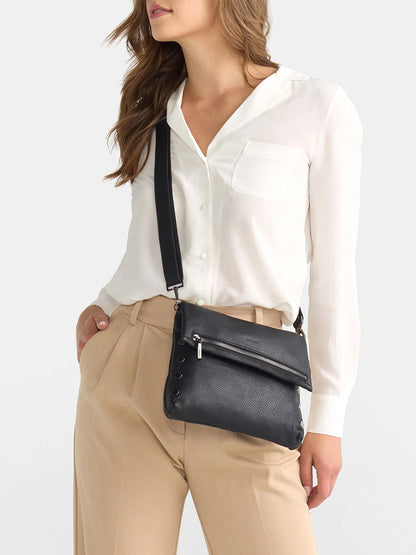 A person in a white blouse and beige trousers is wearing the Hammitt Los Angeles VIP Medium Clutch in Black. This versatile bag features an adjustable crossbody strap, making it perfect for adapting to any outfit or occasion.