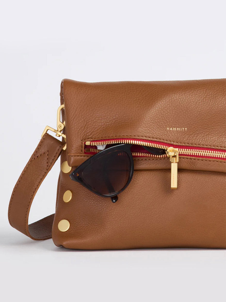 The Hammitt Los Angeles VIP Medium Clutch in Mahogany Pebble boasts a sophisticated pebbled texture and includes a zipper pocket perfect for storing a pair of black sunglasses. The handbag is elegantly adorned with brushed gold rivets and hardware accents.